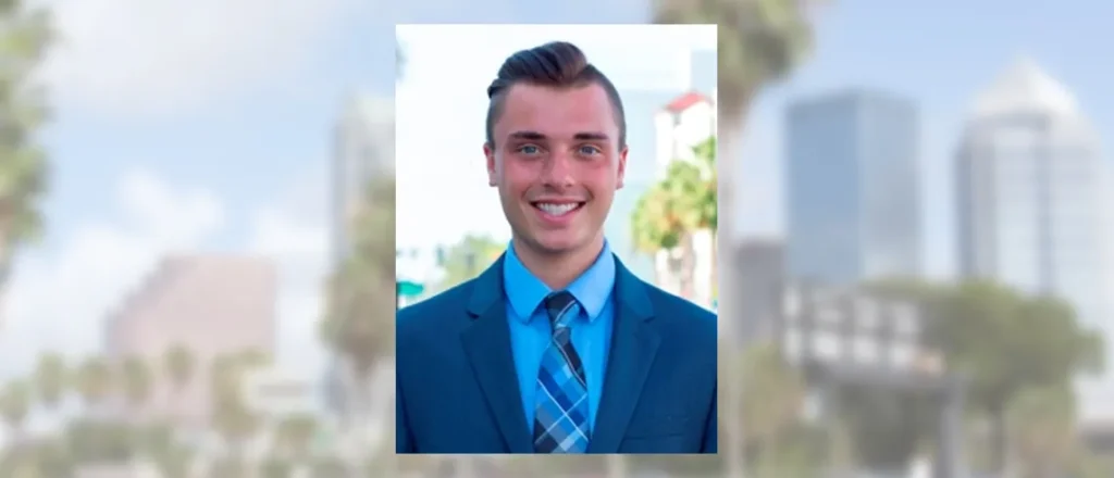 Smiling young man in a blue suit and tie with the Tampa skyline blurred behind him