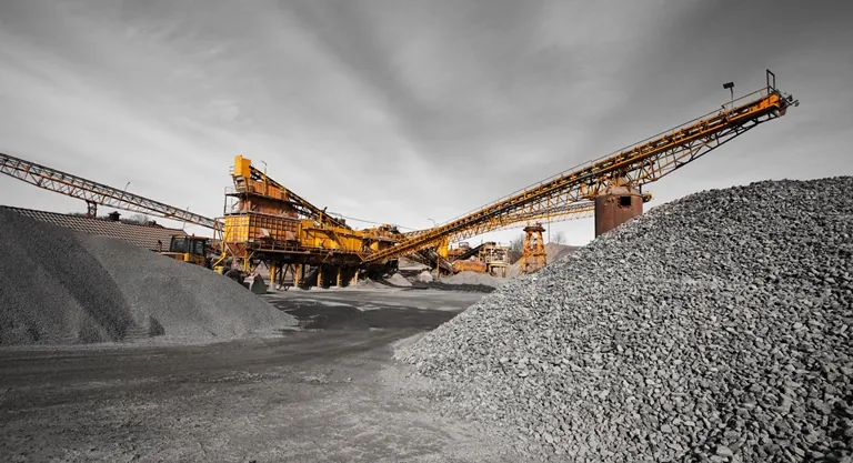Orange conveyor equipment beside a large gravel pile with a gray cloudy sky behind