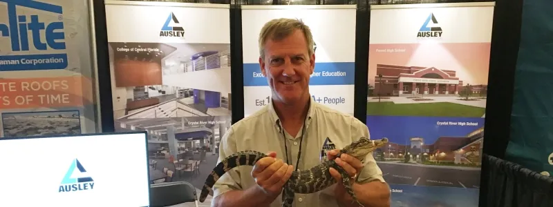 Todd Duffy holding a small alligator in front of the Ausley trade show booth at the FEFPA Summer Conference