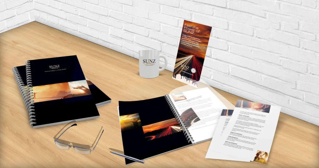 Sunz branded notebooks, mug, glasses and printed folder on a wooden surface