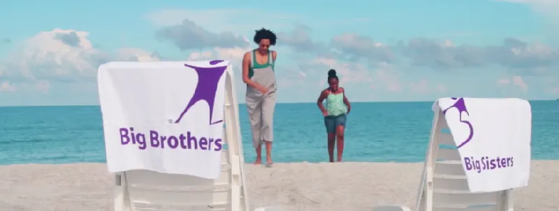 Big Brothers Big Sisters banner on a beach with two people in the back