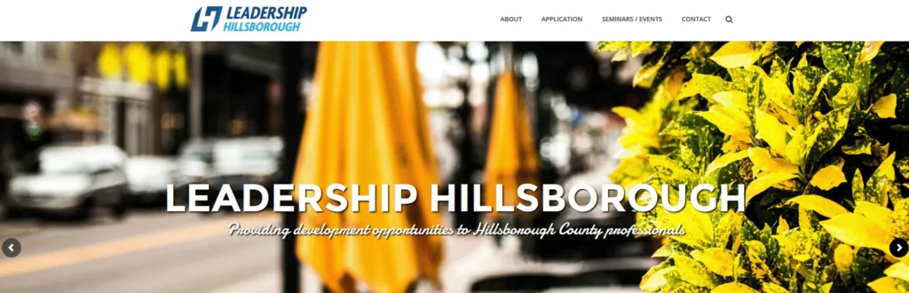 Leadership Hillsborough website header over a blurred street scene with yellow umbrellas