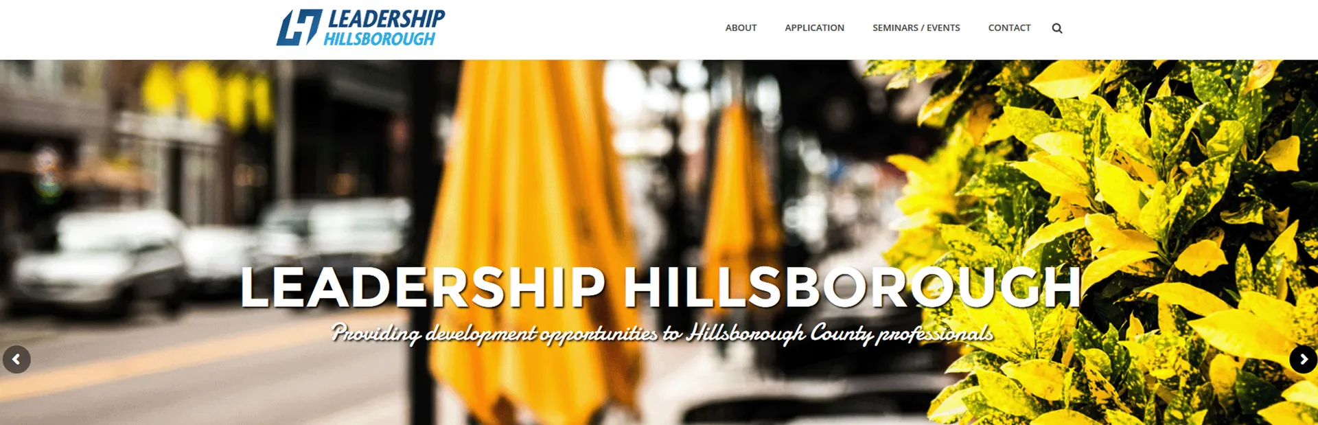 Leadership Hillsborough website header over a blurred street scene with yellow umbrellas