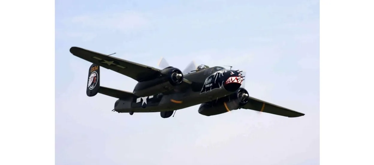 Black twin engine propeller warbird airplane flying against a pale sky