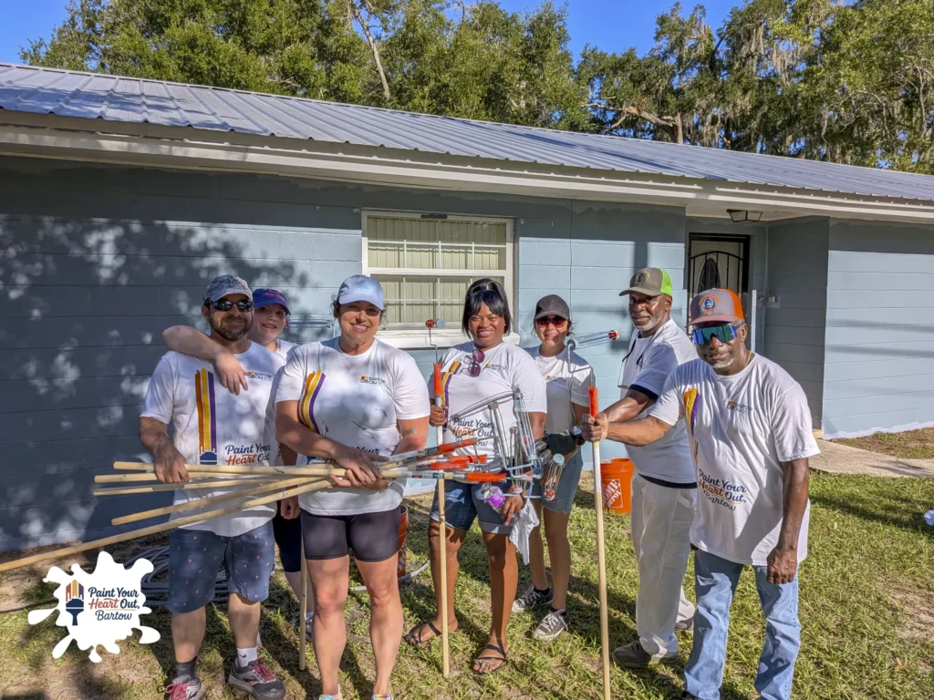 Group of volunteers with paint poles in front of a blue gray house