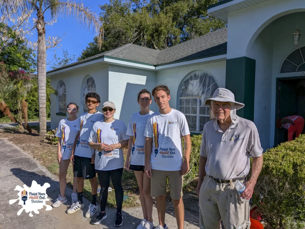 Volunteers and an older man in a hat in front of a light blue house