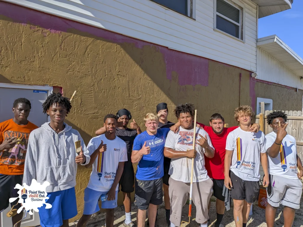 Group of young volunteers holding paint tools in front of a house with fresh brown paint