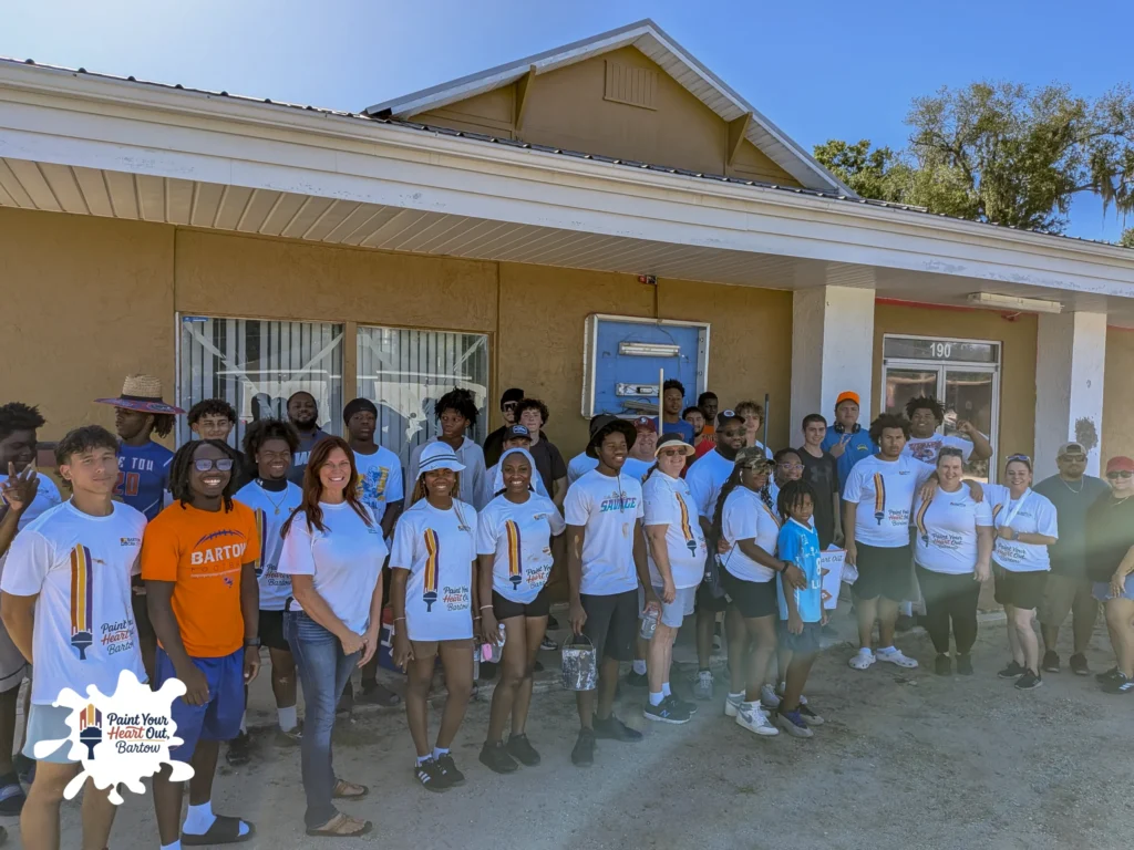 Large group of volunteers in matching shirts in front of a tan house