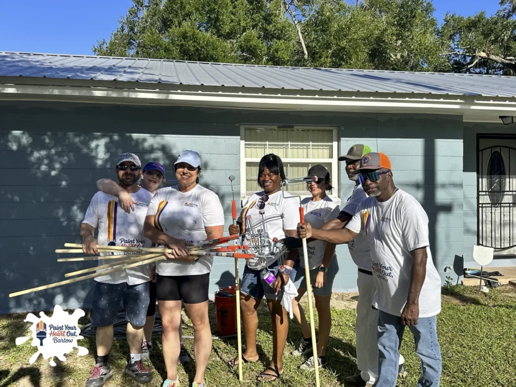 Volunteers holding paint tools in front of a blue gray house