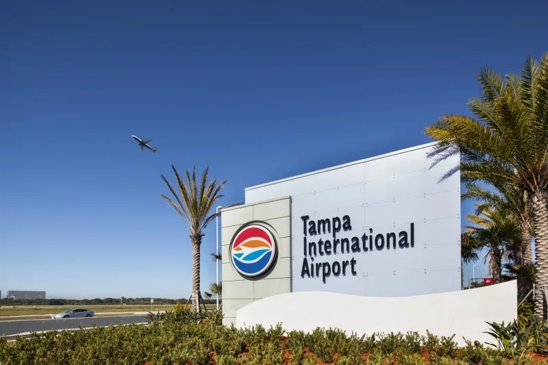 Tampa International Airport sign with palm trees and a plane overhead