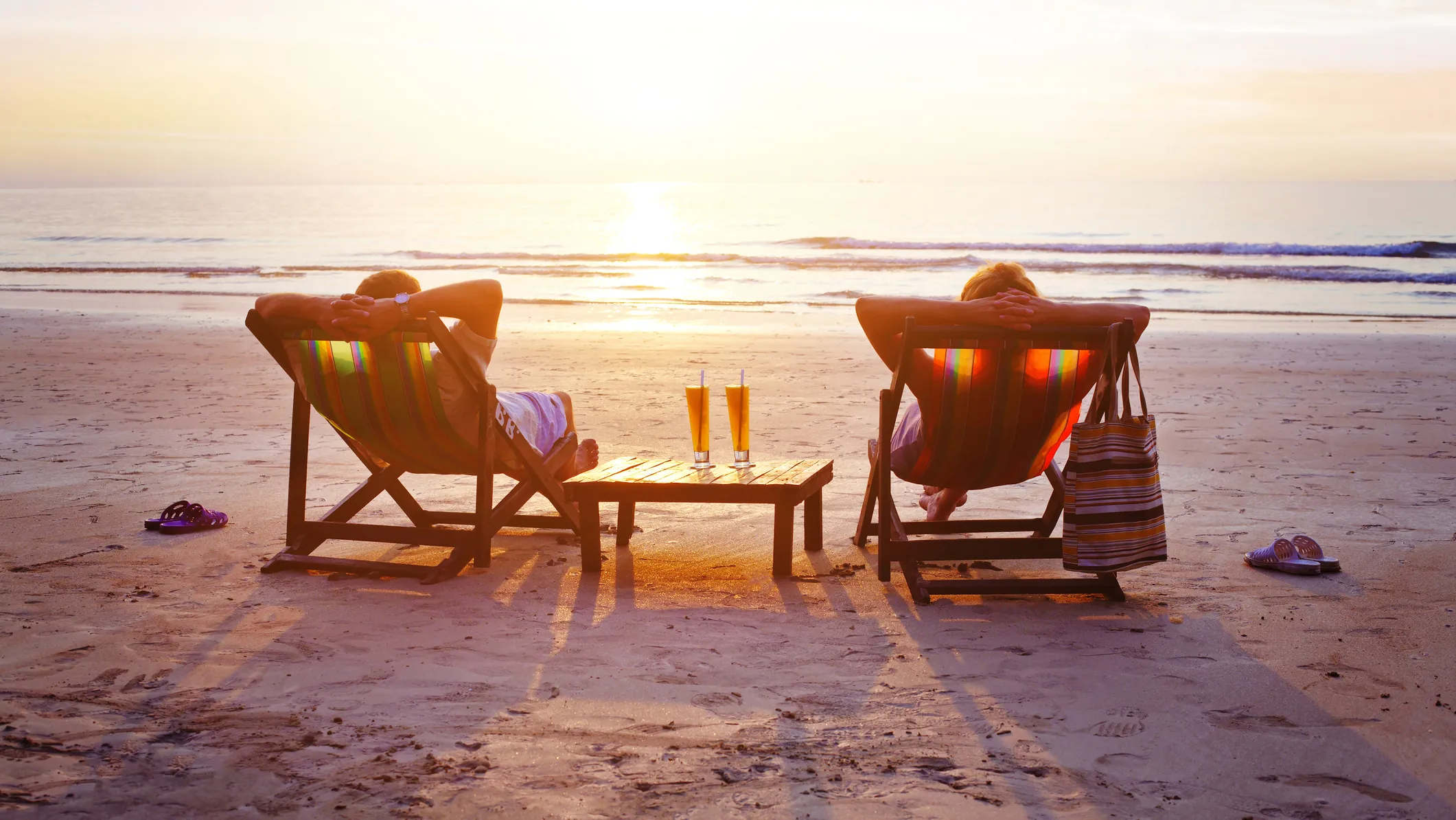 Two people relaxing in beach chairs facing the ocean at sunset