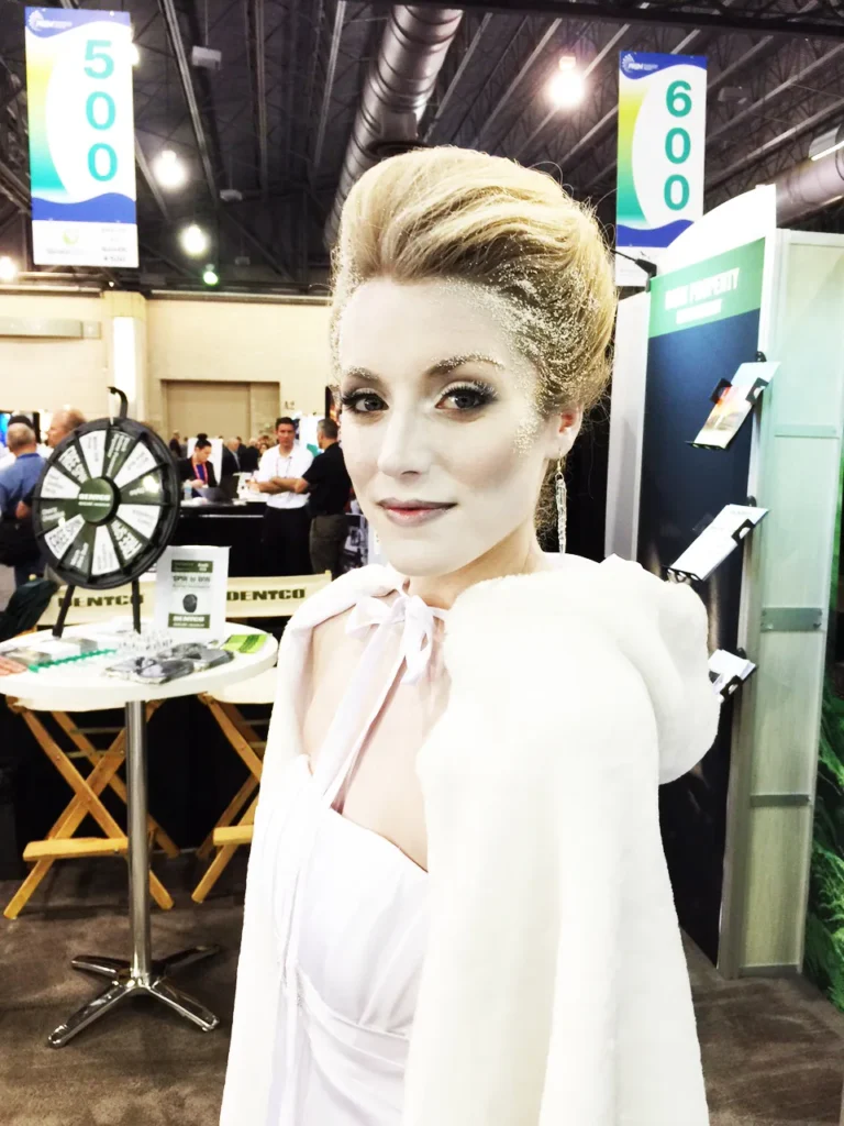 Woman with pale makeup and white cape standing at a trade show booth