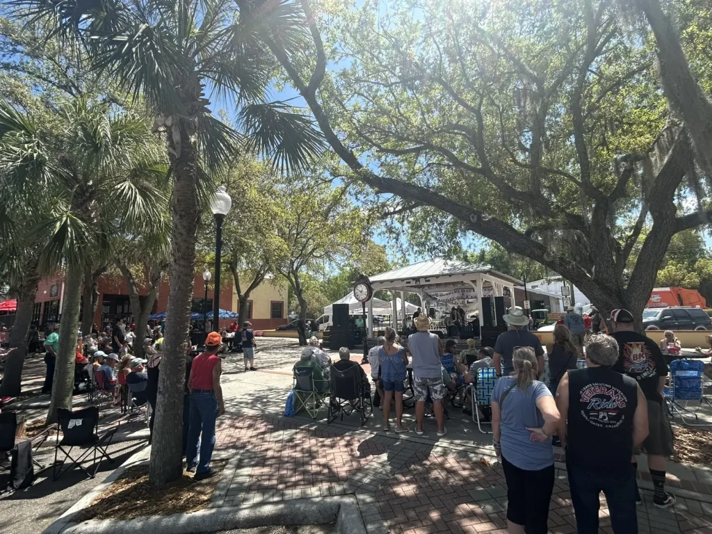 People gathered under shady trees near a stage at a downtown Zephyrhills event