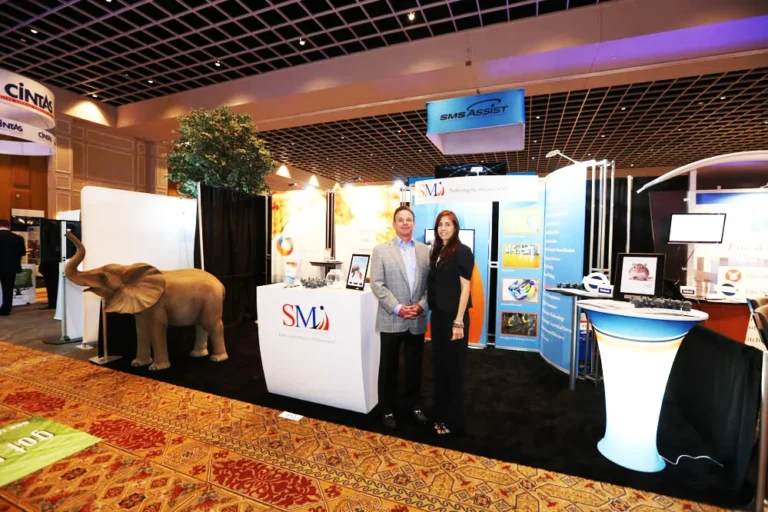 Two people at an SMI trade show booth with elephant figure