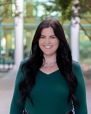 Smiling woman with long dark hair in a green top outdoors