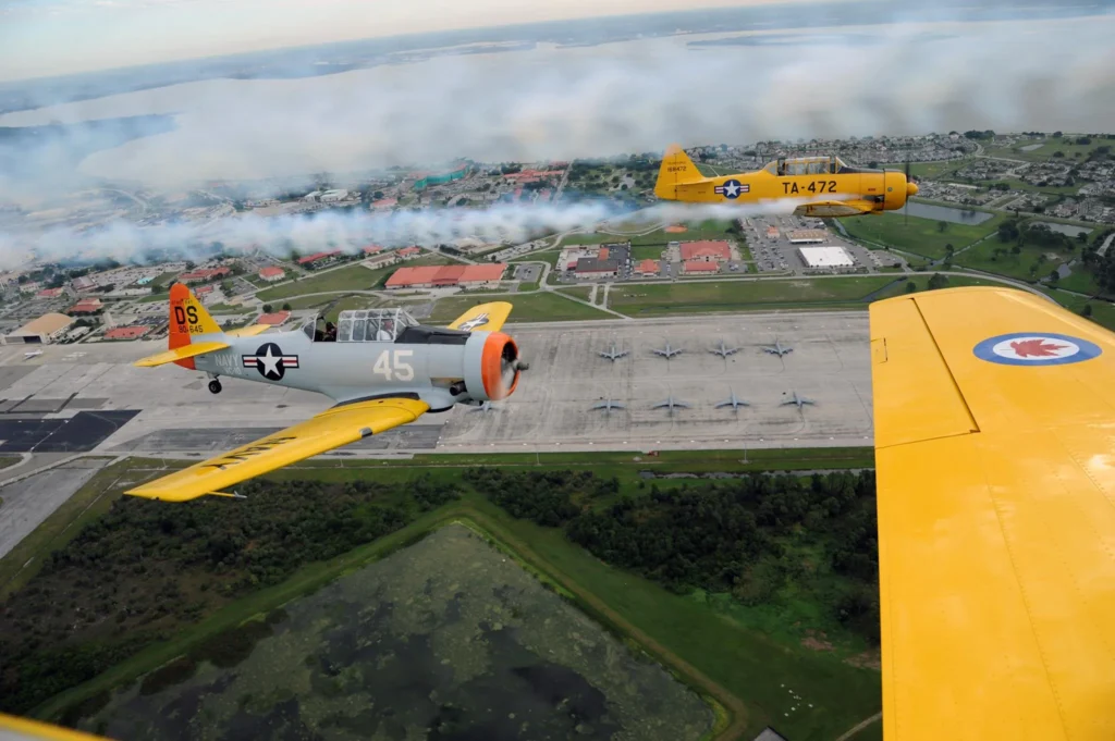 Yellow vintage training aircraft flying in formation over an airfield