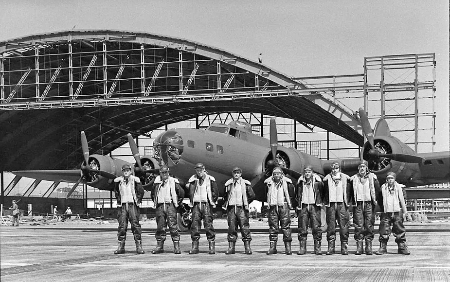 Black and white photo of a B-17 bomber crew lined up in front of a hangar