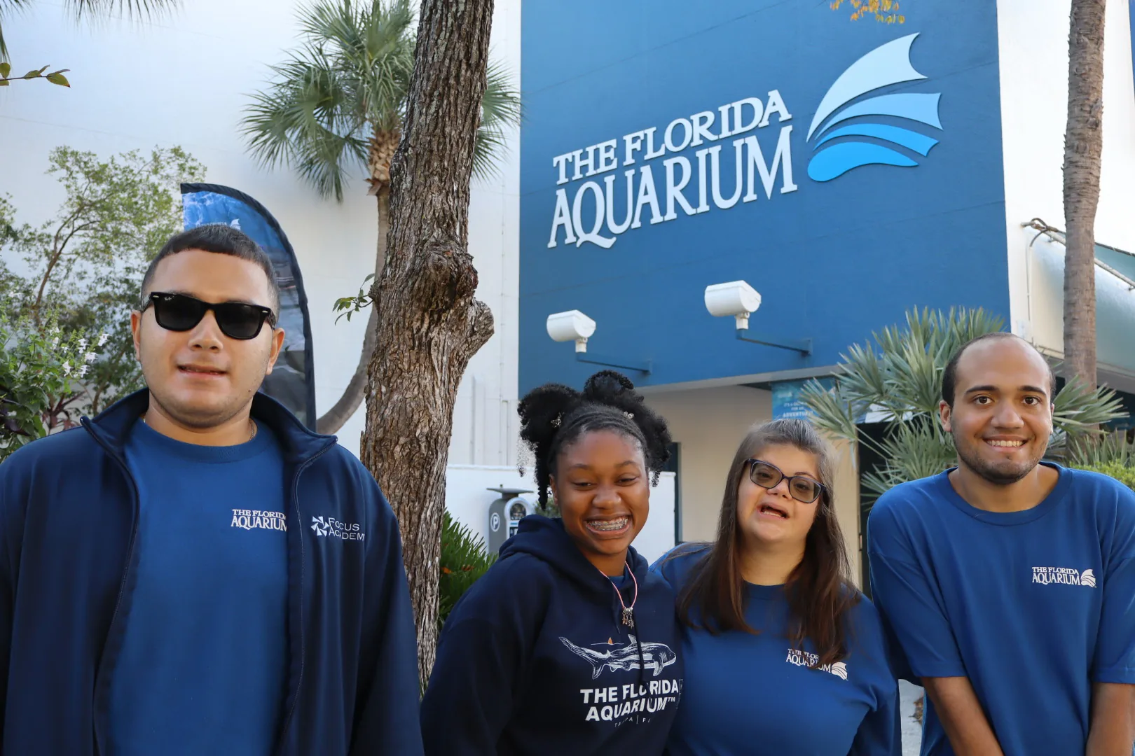 Four people in matching navy shirts in front of The Florida Aquarium sign