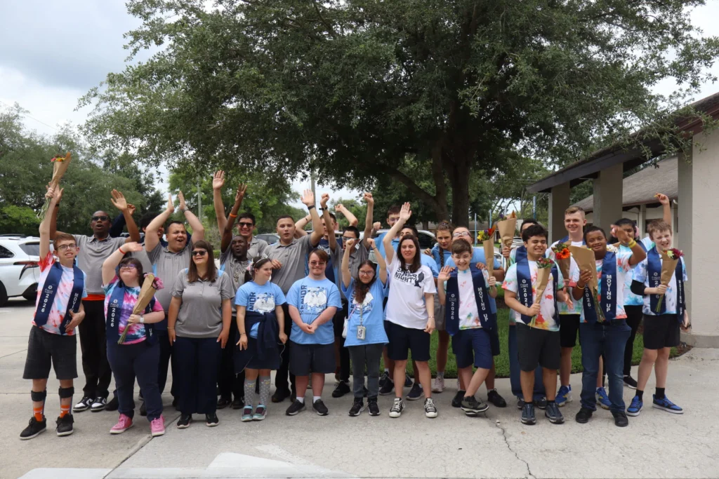Large group of Focus participants and staff raising their hands under a tree