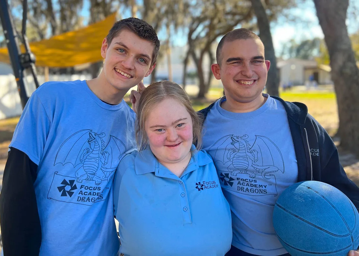 Three smiling young people in blue Focus shirts, one holding a blue ball