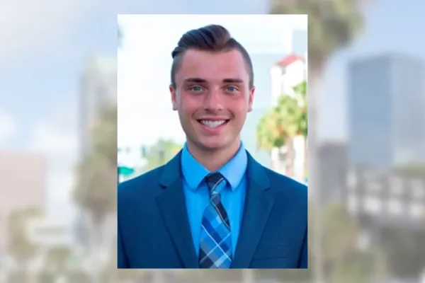 Smiling young man in a blue suit and tie with the Tampa skyline blurred behind him