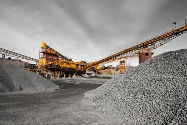 Orange conveyor equipment beside a large gravel pile with a gray cloudy sky behind