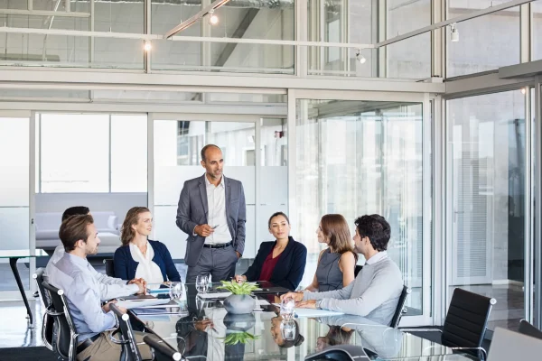 Man standing to address colleagues seated around a table in a glass walled meeting room