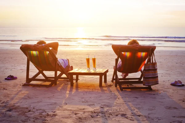 Two people relaxing in beach chairs facing the ocean at sunset