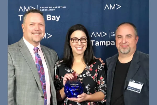 Three people with a blue glass award in front of an American Marketing Association Tampa Bay backdrop