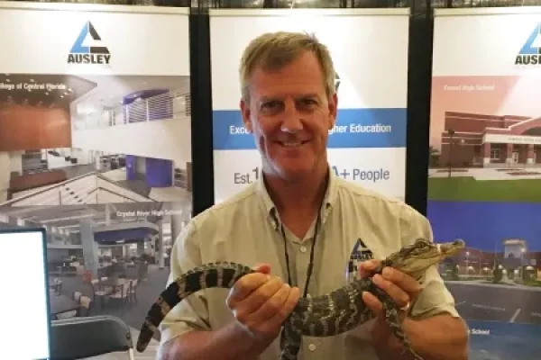 Todd Duffy holding a small alligator in front of the Ausley trade show booth at the FEFPA Summer Conference