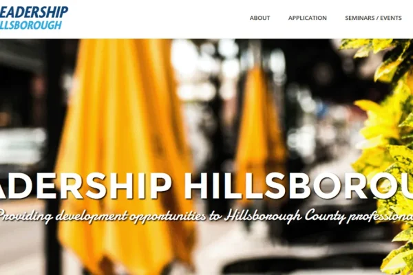 Leadership Hillsborough website header over a blurred street scene with yellow umbrellas