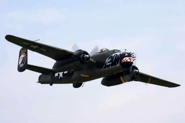 Black twin engine propeller warbird airplane flying against a pale sky